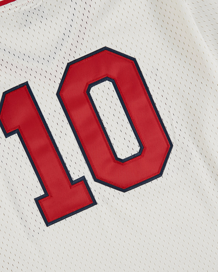 A close-up of the Ebbets Field USA National Team Mesh V-Neck Jersey, featuring white mesh fabric and a red number 10 outlined in dark blue, evoking a vintage baseball style.