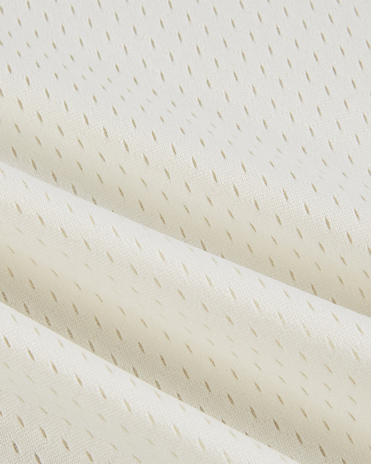 Close-up of the Ebbets Field USA National Team Mesh V-Neck Jersey in light cream, featuring a subtle diagonal perforated pattern and soft folds, evoking the textured look of a vintage baseball jersey.