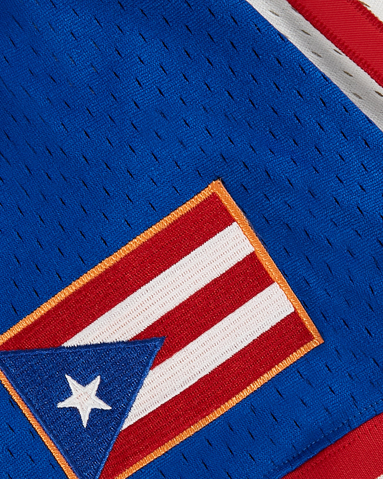 A close-up of the Puerto Rican flag patch on the blue mesh fabric of the Ebbets Field Puerto Rico 1976 National Team Mesh V-Neck Jersey, featuring small perforations and red and white trim for a vintage team look.
