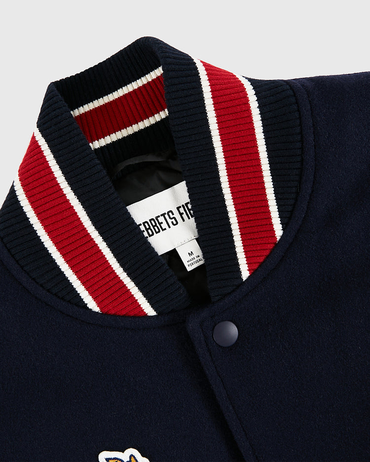 Close-up of the USA 1960 Miracle On Ice All-Wool Varsity Jacket by Ebbets Field, featuring a navy body, ribbed red, white, and navy collar, black snap buttons, and an Ebbets Field inside label.