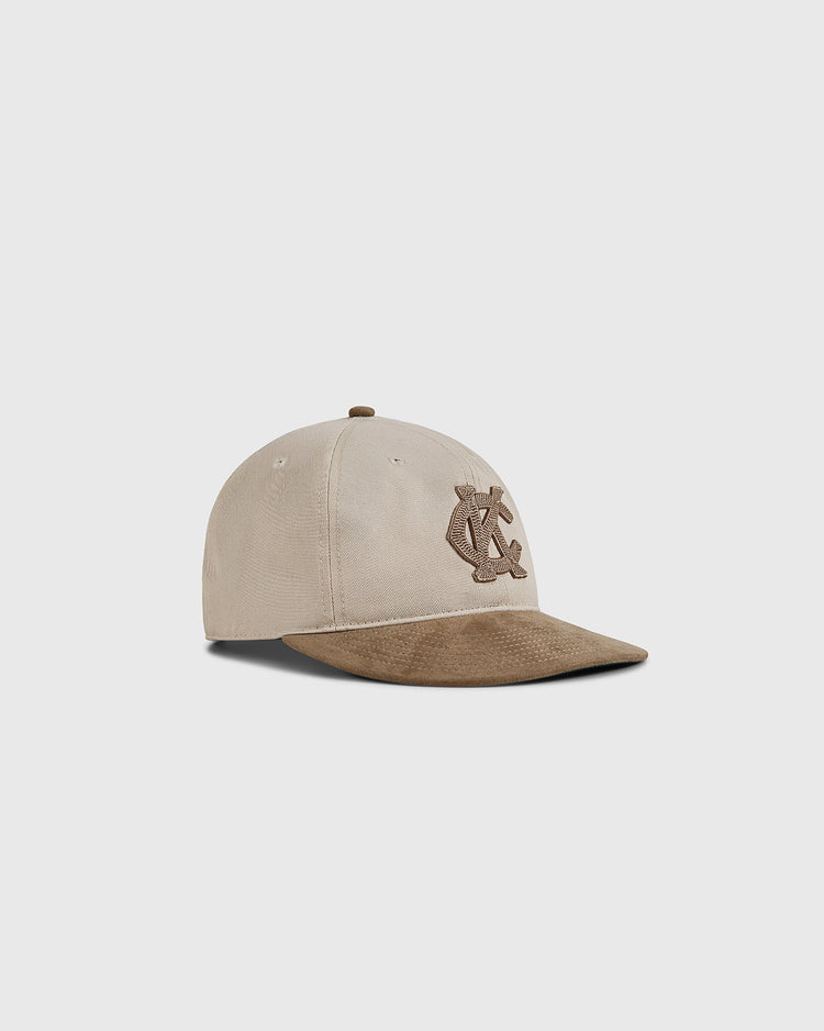 The Ebbets Field Kansas City Monarchs 1945 Cotton Twill Suede Ballcap features beige cotton, a brown suede brim, and an embroidered brown C and L logo on the front, shown on a plain light gray background.