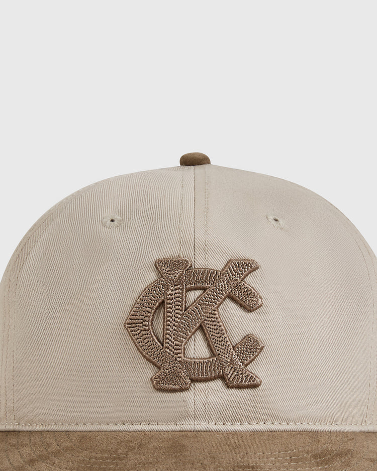 The Ebbets Field Kansas City Monarchs 1945 Cotton Twill Suede Ballcap features a beige crown, brown suede brim, and embroidered “KC” logo, inspired by classic Negro Leagues hats.