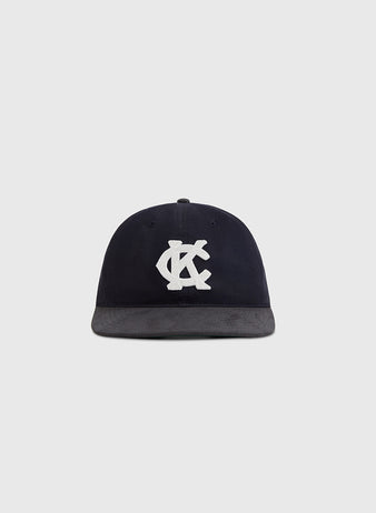 The Kansas City Monarchs 1945 Cotton Twill Suede Ballcap by Ebbets Field features a black flat brim and bold white interlocking KC letters on the front, shown against a plain light gray background.