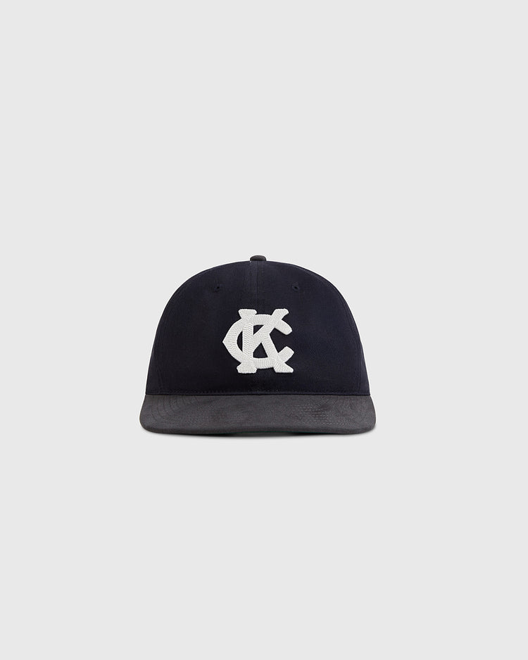 The Kansas City Monarchs 1945 Cotton Twill Suede Ballcap by Ebbets Field features a black flat brim and bold white interlocking KC letters on the front, shown against a plain light gray background.