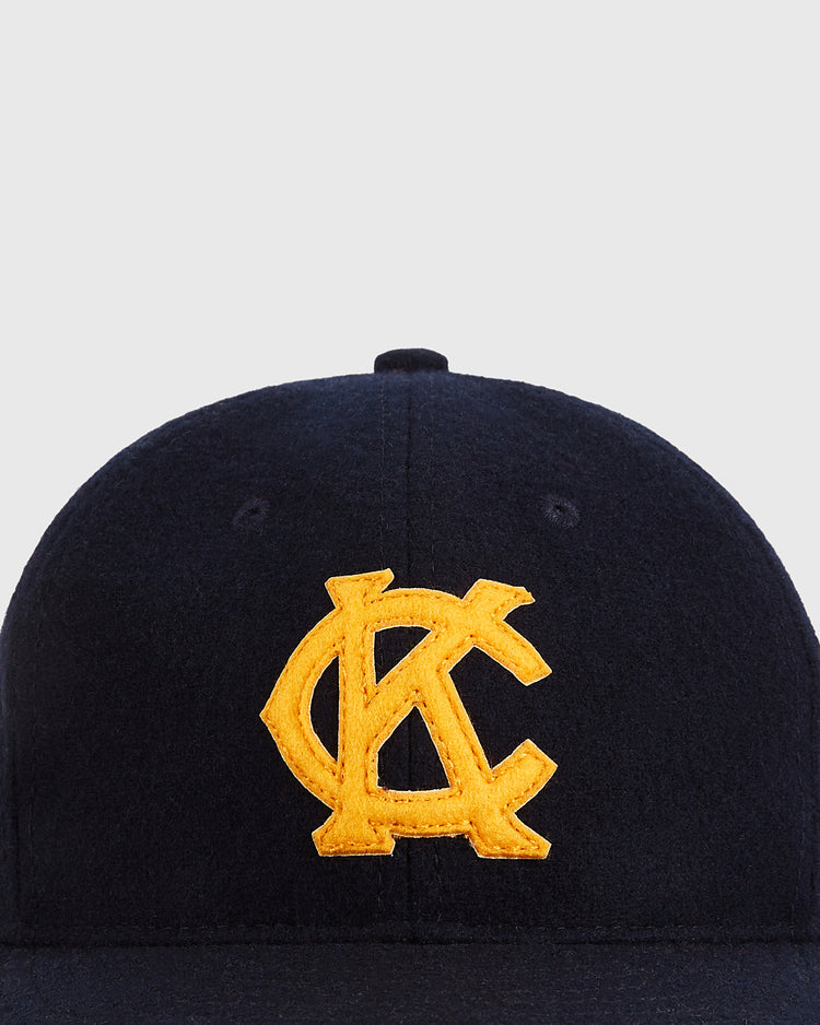 The Ebbets Field Kansas City Monarchs 1945 Authentic Wool Ballcap features bold, overlapping yellow KC embroidery on dark navy wool, inspired by the historic Negro Leagues cap, shown against a plain light gray background.