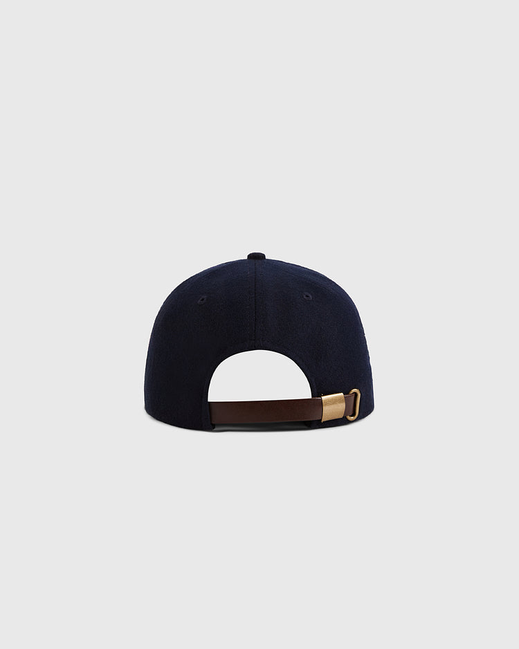 The Ebbets Field Kansas City Monarchs 1945 Authentic Wool Ballcap in navy blue is shown from the back, highlighting its brown adjustable strap with a brass buckle against a plain light gray background.