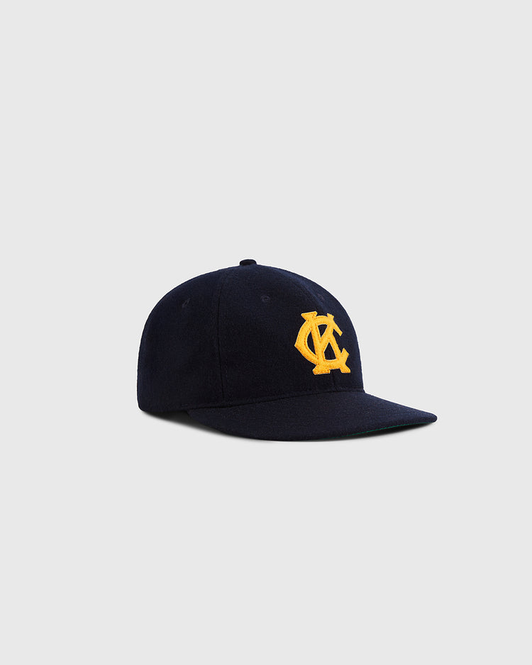The Ebbets Field Kansas City Monarchs 1945 Authentic Wool Ballcap features navy blue wool and a yellow embroidered interlocking YC logo, reminiscent of the classic team cap, shown on a light gray background.