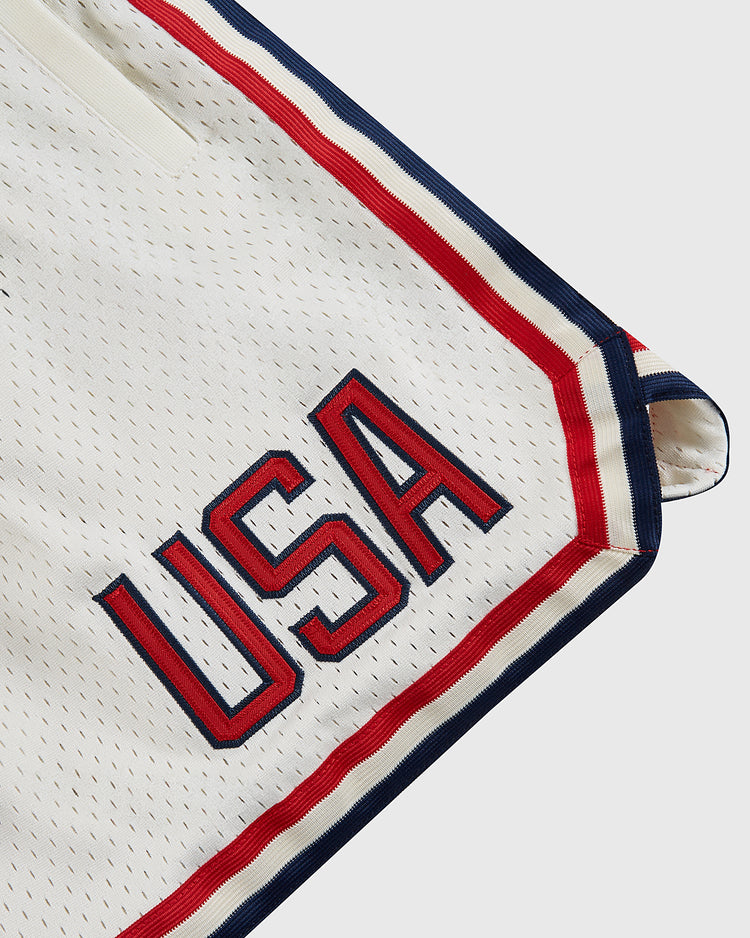 Close-up of Ebbets Field USA National Team Mesh Shorts in white mesh with red and blue trim, inspired by the 1956 Olympics and featuring bold embroidered USA lettering near the hem.