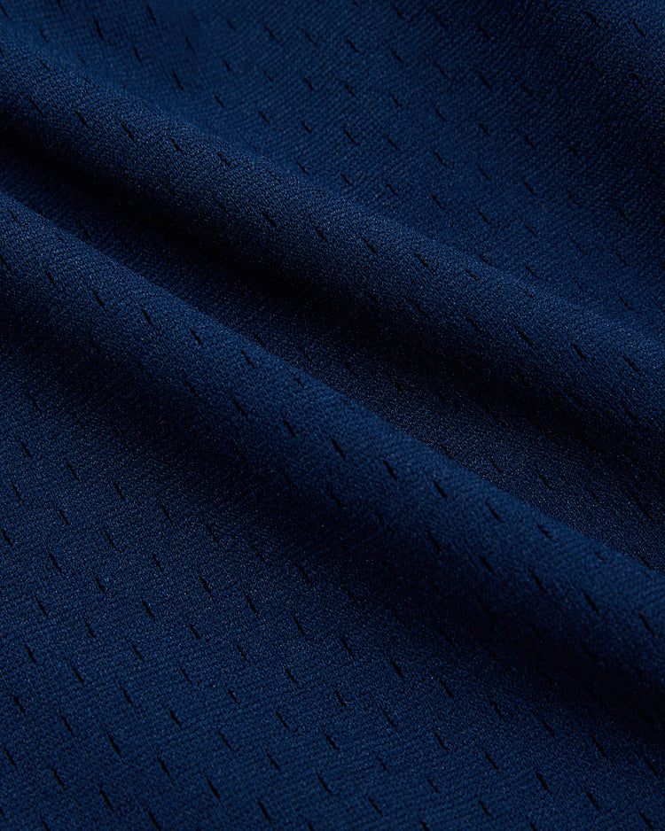 Close-up of the dark blue, breathable knit mesh fabric of Ebbets Field's USA National Team Mesh Shorts, featuring a subtle dotted texture and gentle diagonal folds.