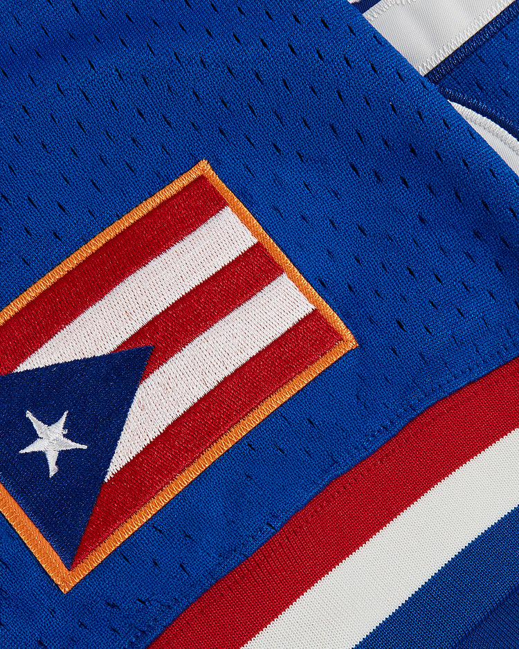 Close-up of the Ebbets Field Santurce Cangrejeros mesh V-neck jersey, showcasing Puerto Rican flag patch and red, white, and blue stripes along the edge.