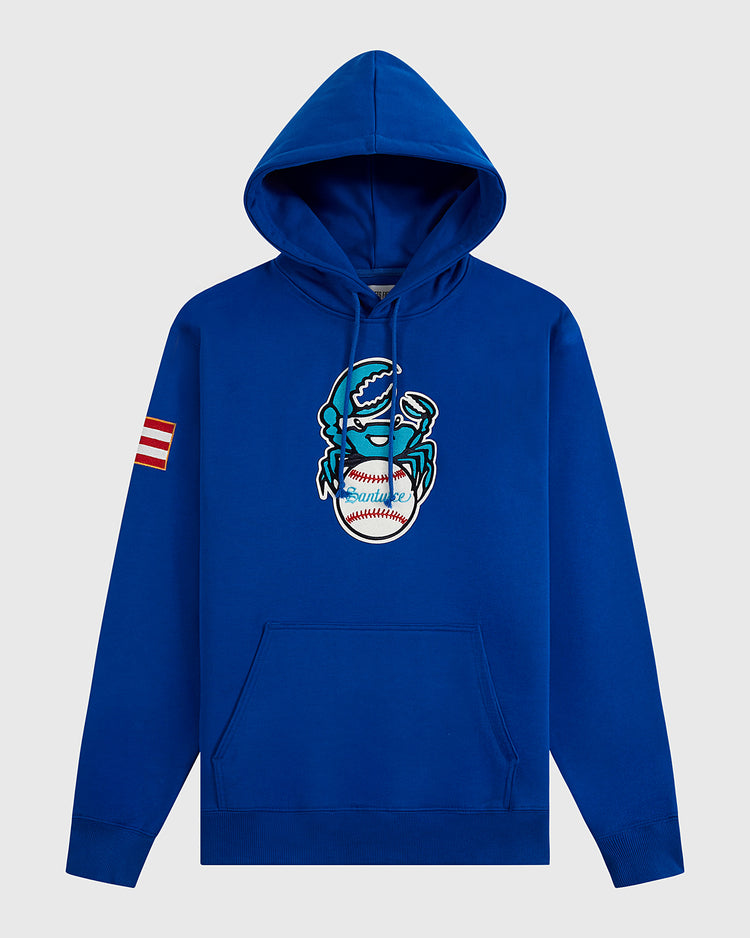 The Ebbets Field Santurce Cangrejeros Heavyweight Cotton Pullover Hoodie features a blue design with a cartoon crab holding a baseball on the front, red-and-white striped sleeve patch, front pocket, and drawstrings—Puerto Rican baseball-inspired.