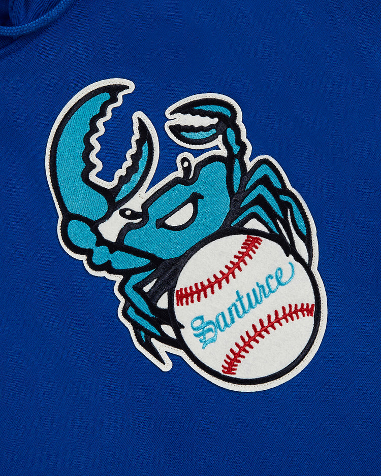 A blue cartoon crab grips a white baseball with “Santurce” in teal on a royal blue background—ideal for fans and perfect on the Ebbets Field Santurce Cangrejeros Heavyweight Cotton Pullover Hoodie.