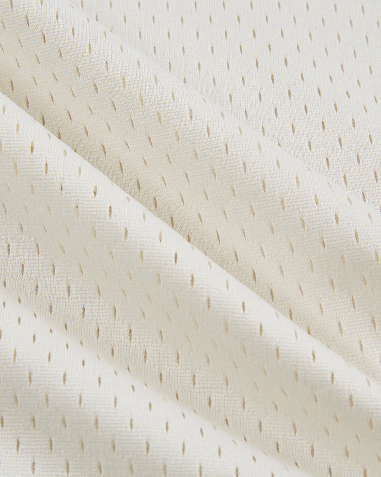 Close-up of the Ebbets Field Diablos Rojos de Mexico V-Neck Mesh Jersey, showing cream-colored, perforated, textured fabric with diagonal folds—soft and breathable material ideal for sportswear.