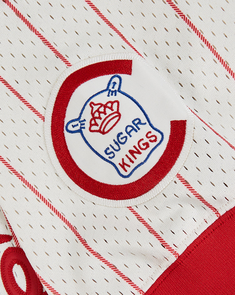 Close-up of the Ebbets Field Havana Cubans Mesh V-Neck Jersey in white with red pinstripes, featuring a circular SUGAR KINGS patch with a blue sugar sack and red crown—honoring the legacy of the Havana Cubans.