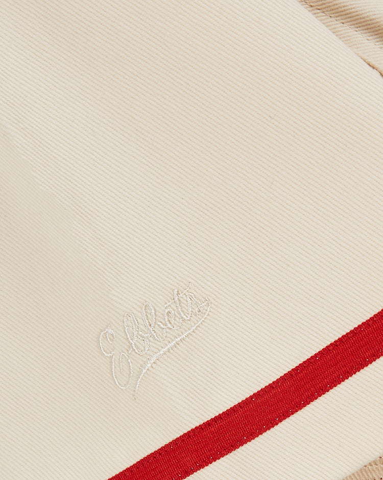 A close-up of Ebbets Field’s Diablos Rojos del Mexico cotton twill baseball jersey, featuring cream fabric with a subtle “Elliot” embroidered script logo and a bold red stripe, inspired by classic Mexican baseball style.