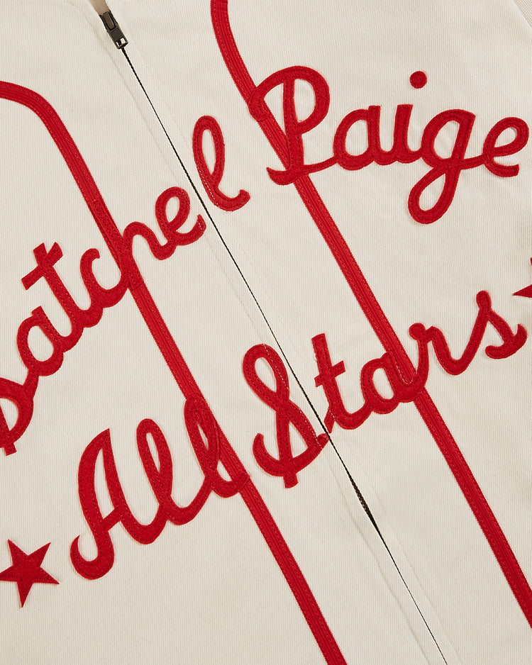 A close-up of the Ebbets Field Satchel Paige All-Stars 1933 Cotton Twill Jersey shows white fabric with bold red cursive embroidery, inspired by the 1933 Pittsburgh Crawfords, and a partially visible vertical zipper.