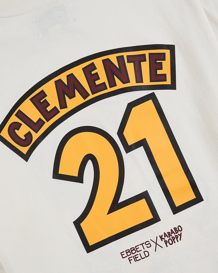 The Karabo Poppy x Ebbets Field Roberto Clemente Short Sleeve Graphic Tee by Ebbets Field features Clemente’s name in yellow and red over the number 21, with the Karabo Poppy and Ebbets Field logos, celebrating his legacy and Black History Month.