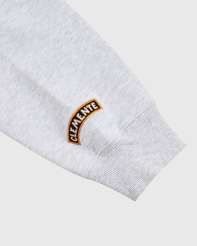 A close-up of the Karabo Poppy x Ebbets Field Roberto Clemente Heavyweight Cotton Pullover Hoodie sleeve shows ribbed cuffs and an embroidered CLEMENTE patch in yellow, black, and orange.