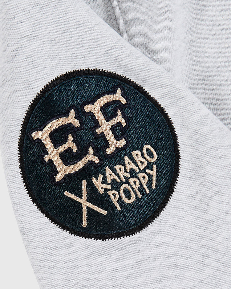 Close-up of the Karabo Poppy x Ebbets Field Josh Gibson Heavyweight Cotton Pullover Hoodie by Ebbets Field, showing gray fabric with a round black patch bearing beige EF letters and 