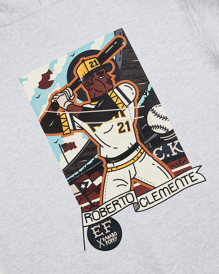 Celebrate Black History Month with the Ebbets Field Karabo Poppy x Roberto Clemente Pullover Hoodie, featuring artwork of Clemente batting in his #21 uniform, stadium and baseball backdrop, and his name displayed at the bottom.