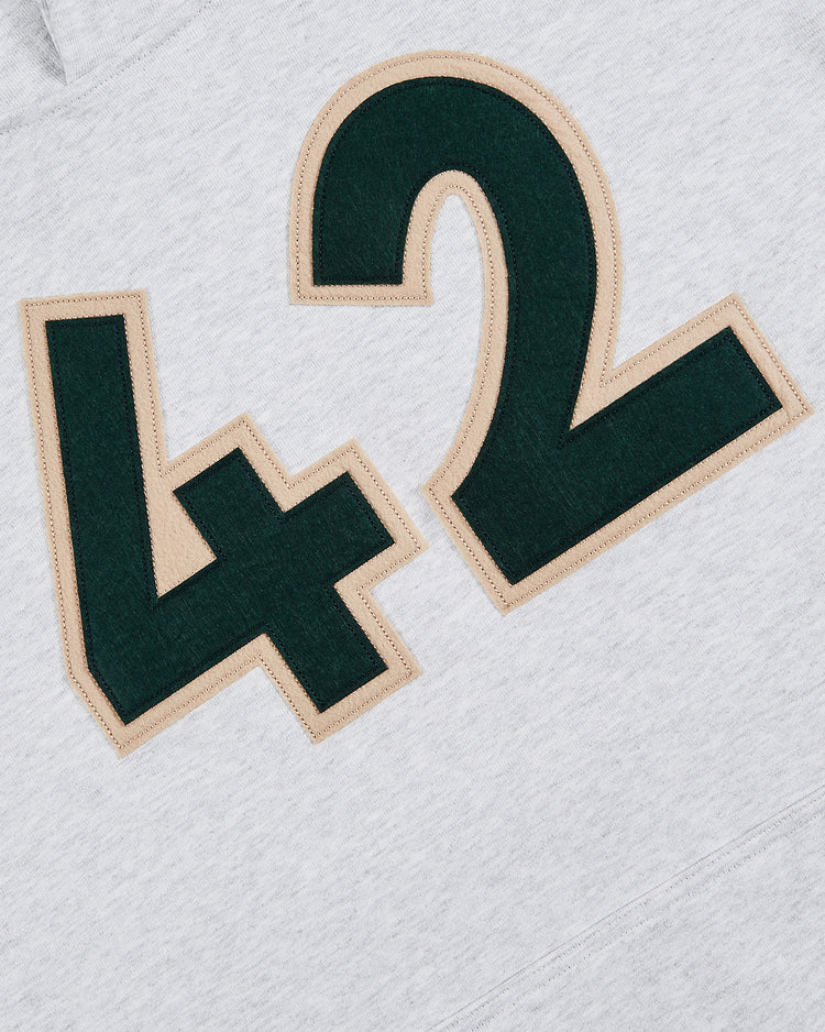 The image features the number 42 in large, dark green and tan outlined letters on light gray fabric from the Ebbets Field Karabo Poppy x Jackie Robinson Heavyweight Cotton Pullover Hoodie.