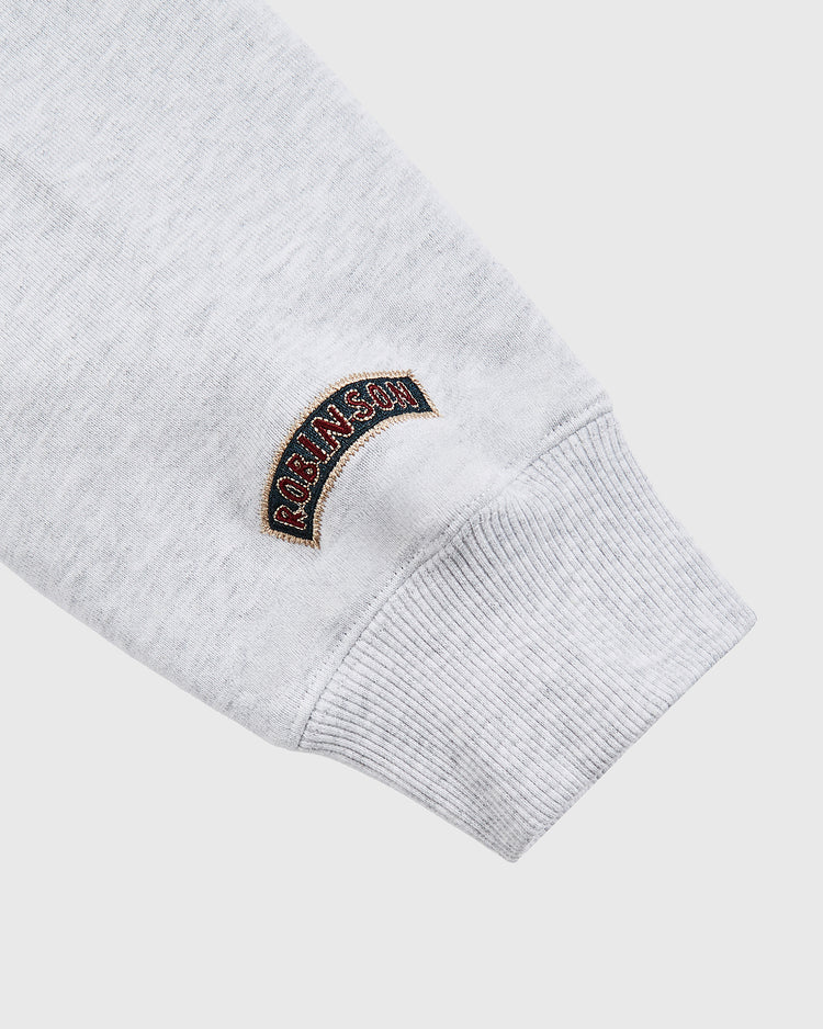 A close-up of a light grey Ebbets Field hoodie sleeve with a ribbed cuff and a small, curved embroidered patch reading ROSHINSON in red, inspired by the Karabo Poppy x Ebbets Field Jackie Robinson Heavyweight Cotton Pullover Hoodie.