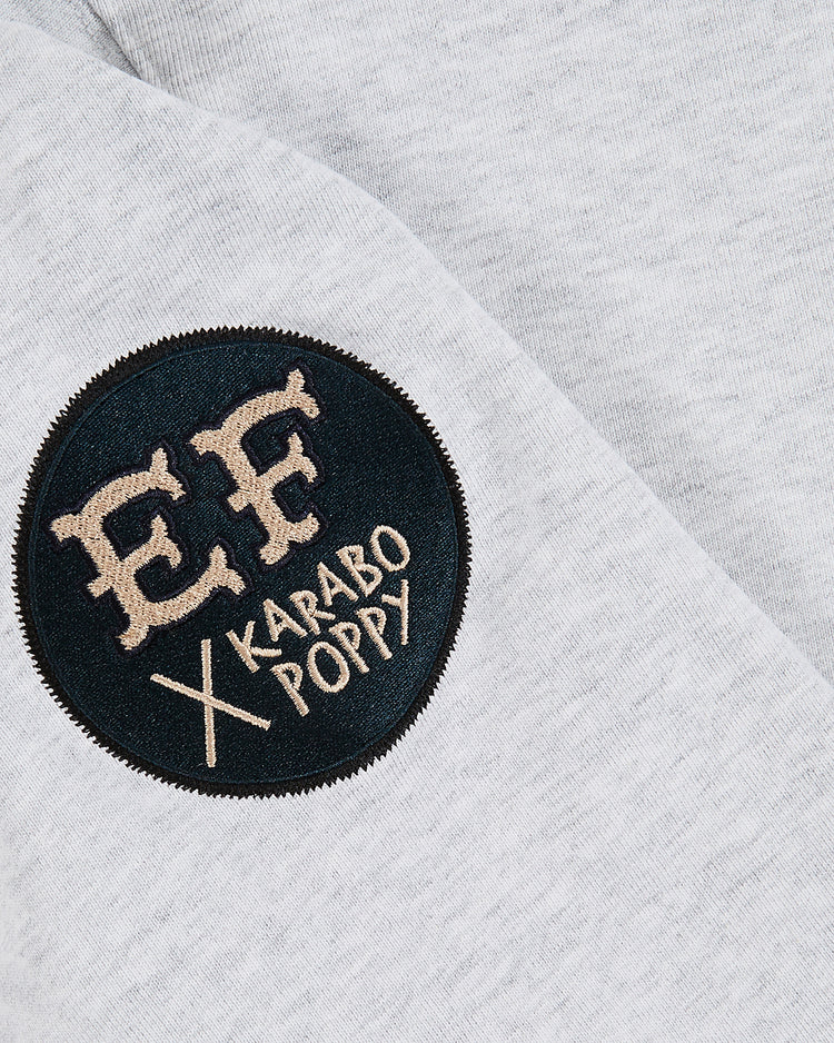 A close-up of the Ebbets Field Karabo Poppy x Ebbets Field Jackie Robinson Heavyweight Cotton Pullover Hoodie shows a grey fabric with a round black patch reading 