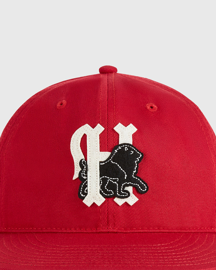 The Ebbets Field Habana Leones Cotton Twill Ballcap features red cotton twill, a black lion patch, and a white stylized letter—ideal for Los Leones de Habana fans. Shown on a plain light gray background.