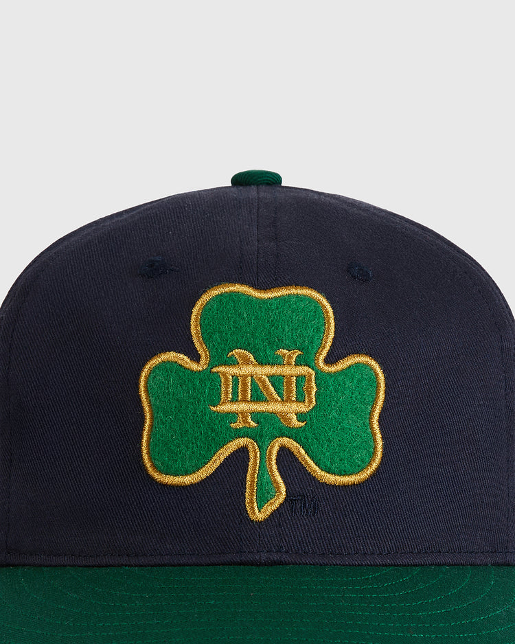 The Ebbets Field University of Notre Dame Shamrock Cotton Twill Ballcap is a navy blue vintage cap with a green shamrock outlined in gold and gold ND lettering embroidered on the front.