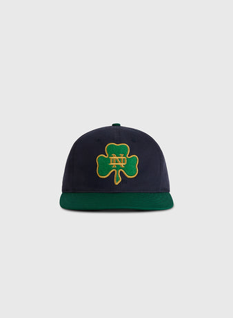 The Ebbets Field University of Notre Dame Shamrock Cotton Twill Ballcap features navy blue cotton twill, a dark green brim, and a green four-leaf clover patch with gold 