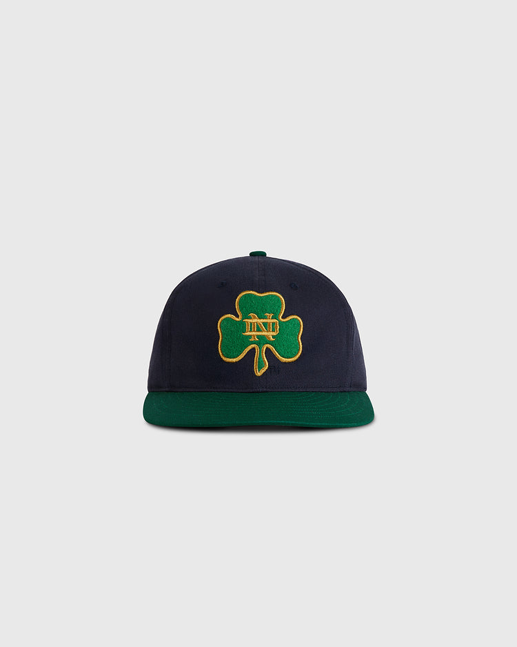 The Ebbets Field University of Notre Dame Shamrock Cotton Twill Ballcap features navy blue cotton twill, a dark green brim, and a green four-leaf clover patch with gold 
