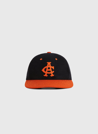 The Ebbets Field Aguilas Cibaenes 1955 Authentic Wool Ballcap features a black crown, orange brim, and orange AC embroidery, inspired by the Dominican winter league, shown on a plain light gray background.