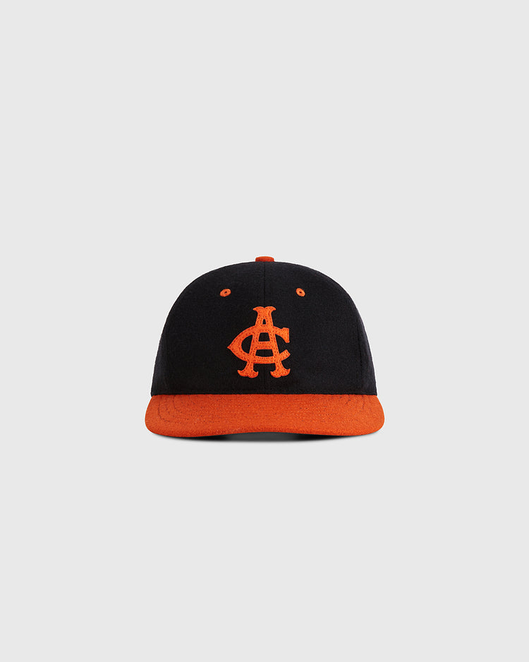 The Ebbets Field Aguilas Cibaenes 1955 Authentic Wool Ballcap features a black crown, orange brim, and orange AC embroidery, inspired by the Dominican winter league, shown on a plain light gray background.
