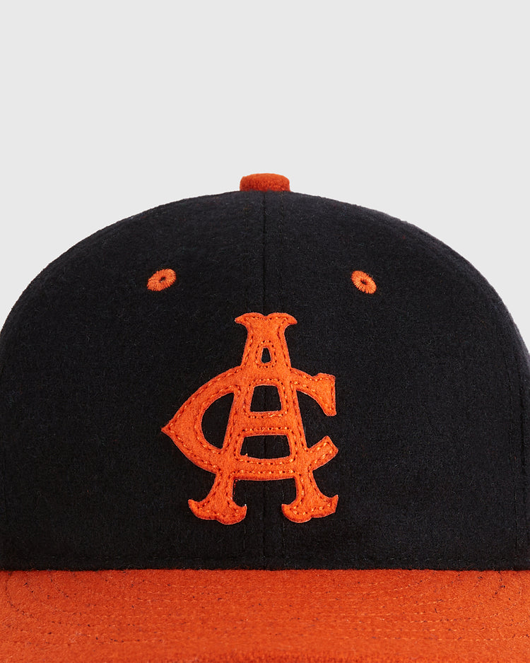 The Ebbets Field Aguilas Cibaenes 1955 Authentic Wool Ballcap features a black crown with orange eyelets, an orange brim and button, and an interlocking orange A and C logo, honoring the Dominican winter league style.