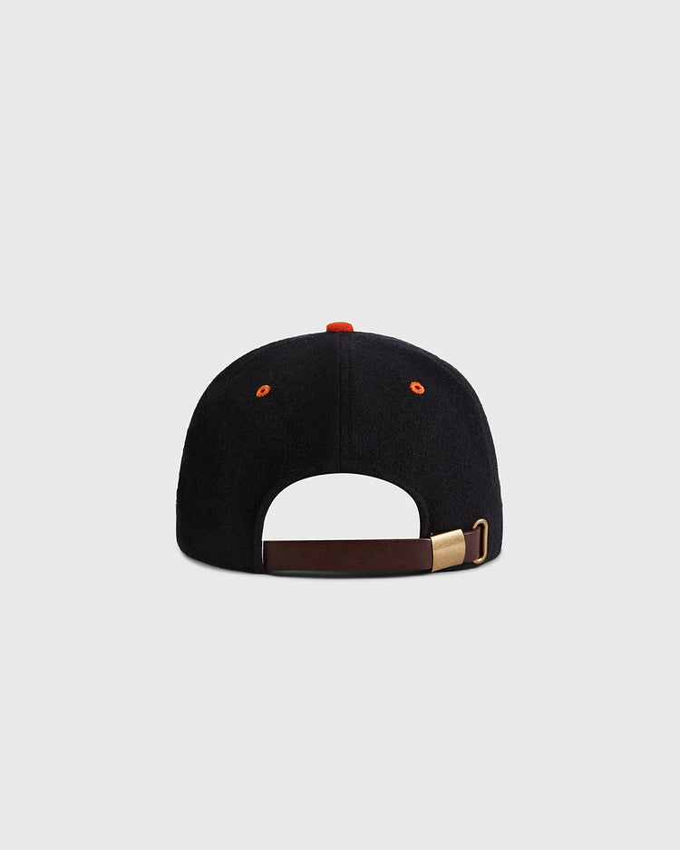 The Aguilas Cibaenes 1955 Authentic Wool Ballcap by Ebbets Field is shown from the back with an orange top button, orange eyelets, and an adjustable brown leather strap with a brass buckle, set against a plain light gray background.