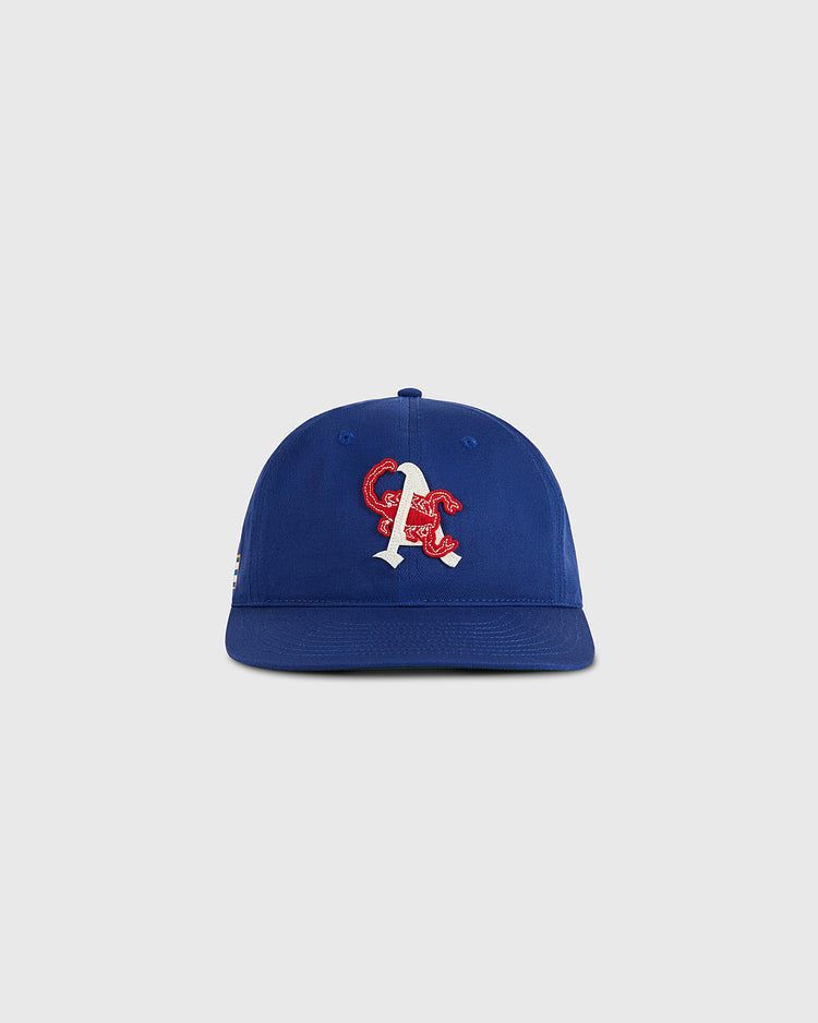 The Ebbets Field Almendares Alacranes Cotton Twill Ballcap is a vintage blue cap with a white and red embroidered “A” and red snake on the front, inspired by Cuban baseball hats. Shown on a plain light gray background.