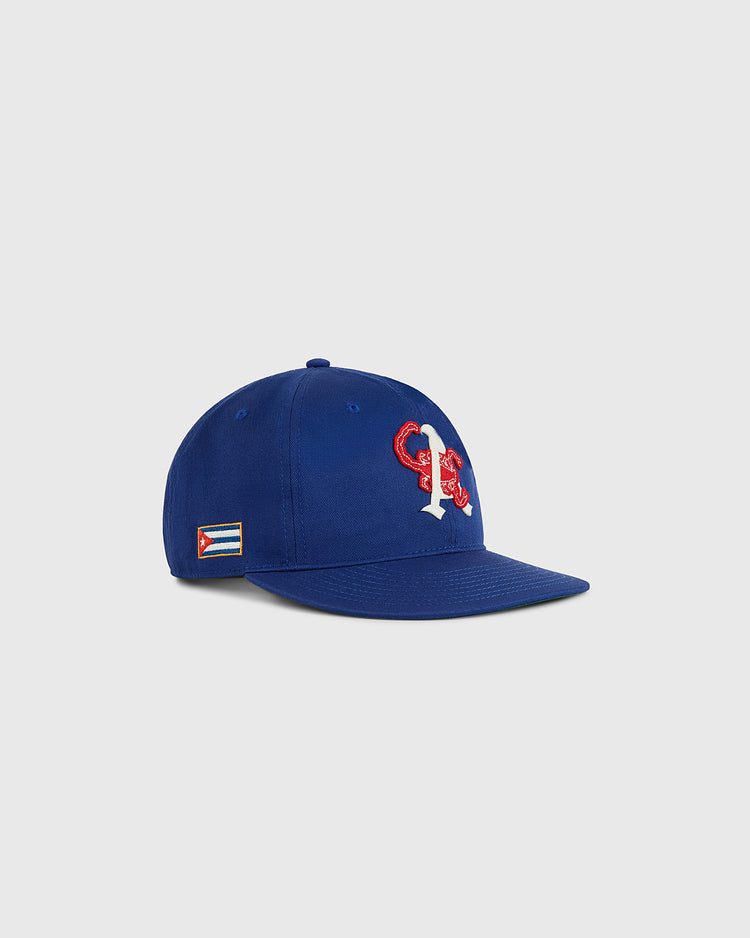 The Ebbets Field Almendares Alacranes Cotton Twill Ballcap is a royal blue vintage-inspired hat with a white and red C and R logo on the front and a Cuban flag patch on the side, shown against a plain light gray background.