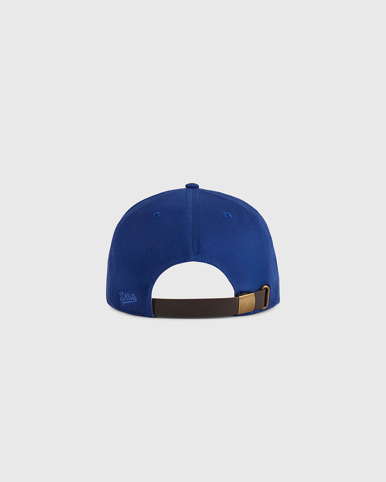 The Almendares Alacranes Cotton Twill Ballcap by Ebbets Field is shown from the back in blue, featuring an adjustable brown strap with a gold buckle. The background is plain light gray.