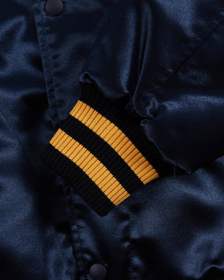 Close-up of the Ebbets Field Notre Dame Satin Varsity Jacket, showcasing its shiny navy blue finish, black cuff with two bold yellow stripes, luxurious texture, and classic button details inspired by vintage varsity style.