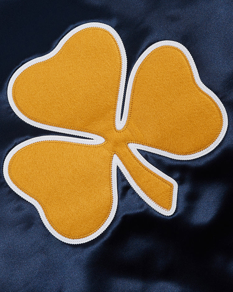 The Ebbets Field Notre Dame Satin Varsity Jacket features a yellow three-leaf clover with a white border stitched onto dark blue shiny fabric, creating a classic, vintage-inspired look.
