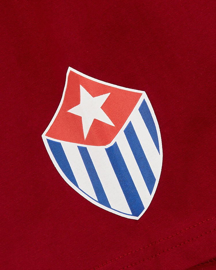 The Ebbets Field Habana Leones Short Sleeve Graphic Tee features a red shield with a white star and blue-white vertical stripes, inspired by Los Leones de Habana from the Cuban League, displayed on red fabric.