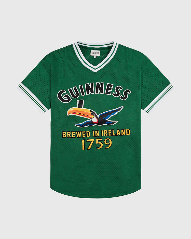 The Ebbets Field Guinness Toucan Mesh V-Neck Jersey is a green short-sleeve top with white trim, featuring a large Guinness logo, colorful toucan with pint, and “Brewed in Ireland 1759” text on the front.