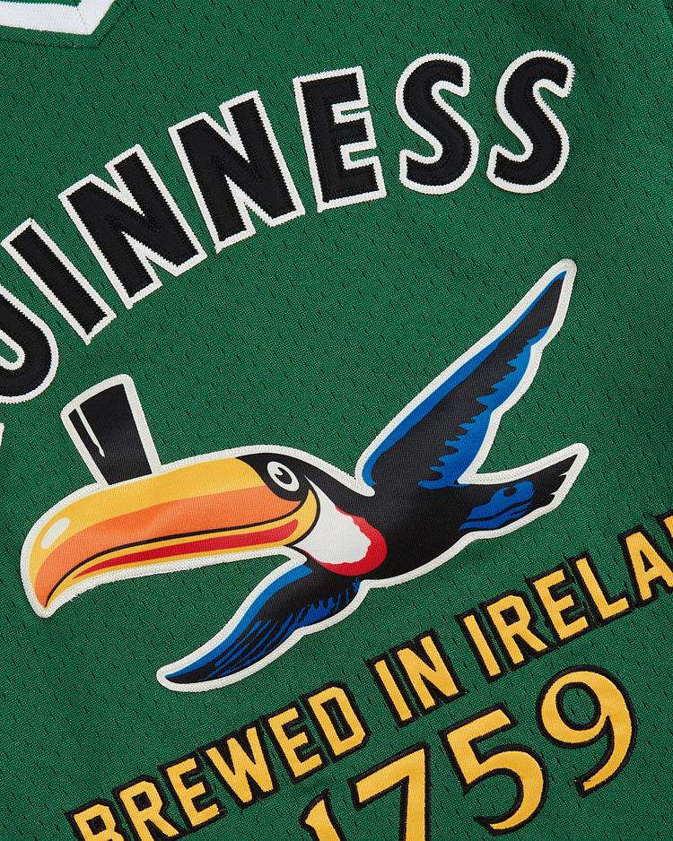 Close-up of the Guinness Toucan Mesh V-Neck Jersey by Ebbets Field, featuring green fabric with the Guinness logo, a colorful flying toucan, and yellow 