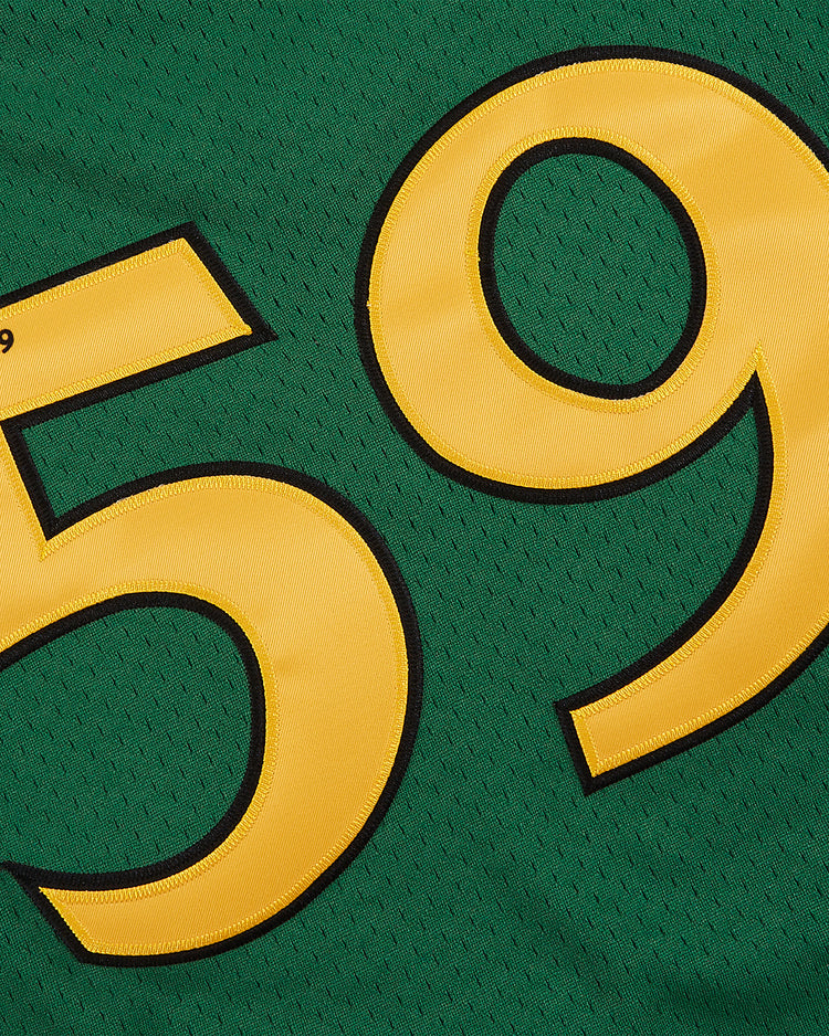 A close-up of the Ebbets Field Guinness Toucan Mesh V-Neck Jersey shows its green mesh fabric with large yellow numbers 59 outlined in black. The breathable material features small holes throughout.
