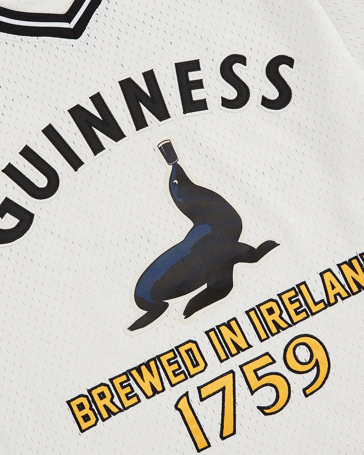 A close-up of the Ebbets Field Guinness Seal Mesh V-Neck Jersey, featuring the Guinness logo, a black seal balancing a bottle, and “Brewed in Ireland 1759” in bold yellow and black.