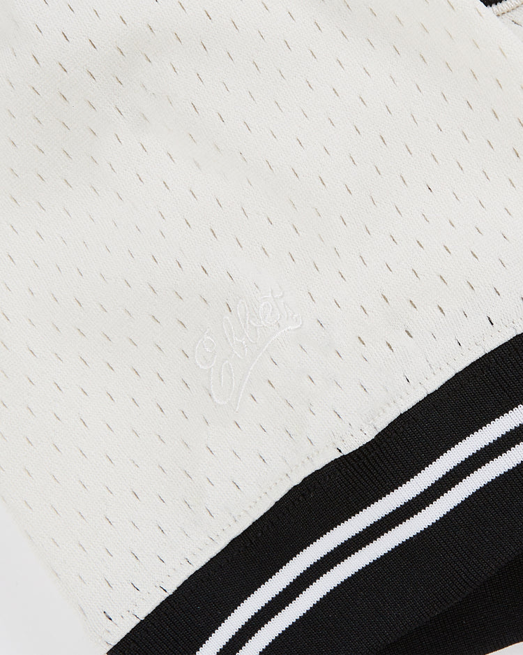Close-up of the Ebbets Field Guinness Seal Mesh V-Neck Jersey shows white mesh fabric with small perforations, subtle white embroidered text, and a black hem accented by two horizontal white stripes.