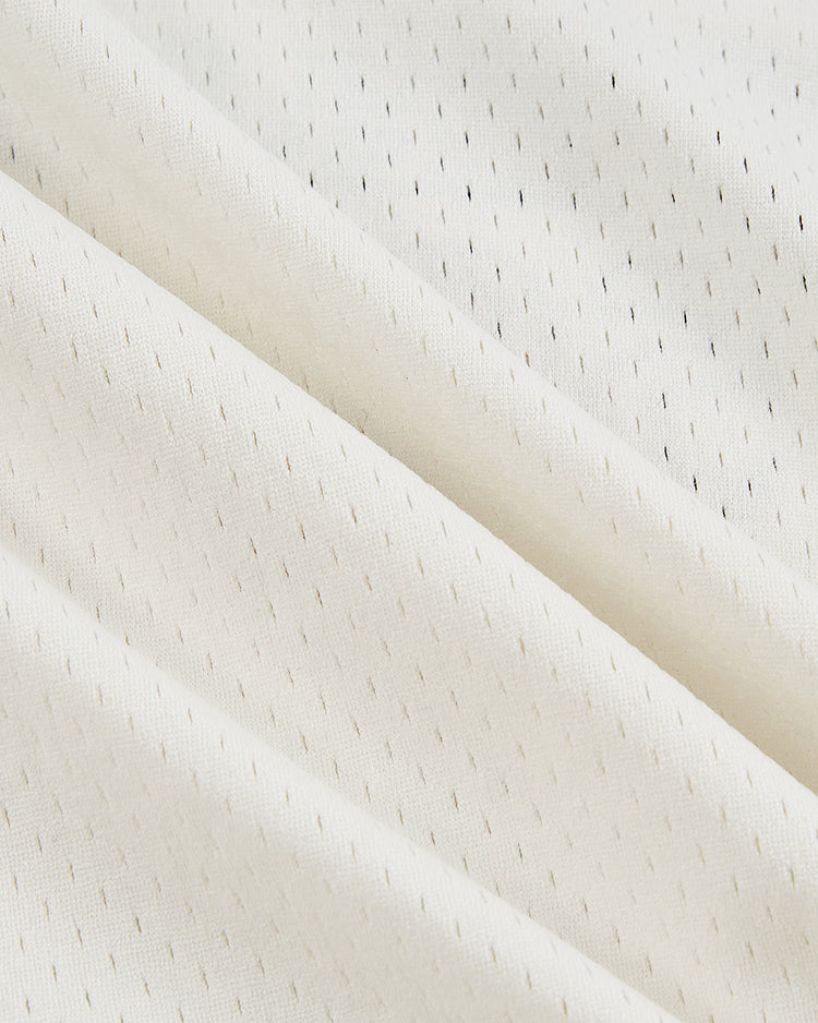 Close-up of the Guinness Seal Mesh V-Neck Jersey by Ebbets Field, featuring cream-colored fabric with small, evenly spaced vertical black dashes and gentle folds that highlight its soft, textured surface.