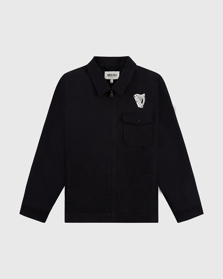 The Guinness Cotton Grounds Crew Jacket by Ebbets Field is a black zip-up with a collar, front chest pocket, and white harp emblem above the pocket, shown on a plain light gray background.