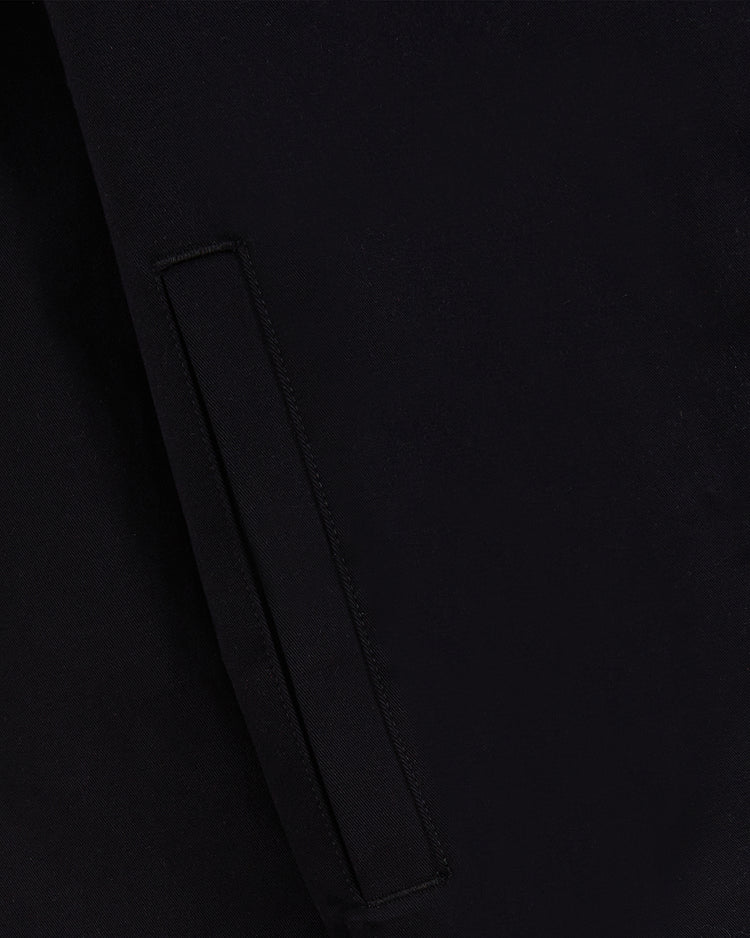 Close-up of the pocket on the Guinness Cotton Grounds Crew Jacket by Ebbets Field, highlighting the black fabric's texture and stitching. The rectangular flap blends into the black background for a seamless look.