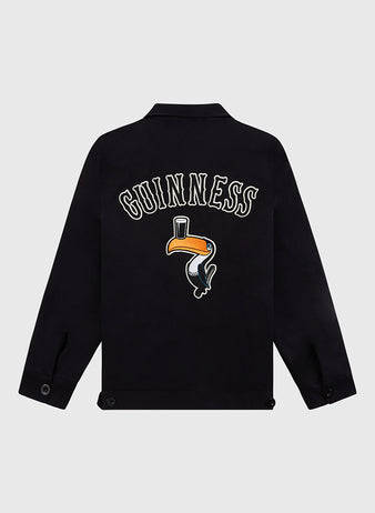 The Guinness Cotton Grounds Crew Jacket by Ebbets Field features “Guinness” in bold white letters above an embroidered toucan balancing a pint on its beak, displayed from the back against a plain light background.